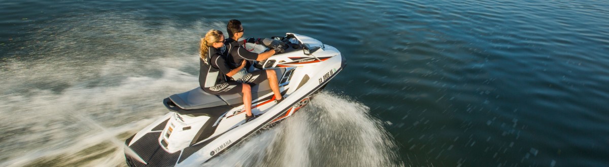 Two people riding on a 2017 Yamaha PWC moving across flat water on a sunny day.